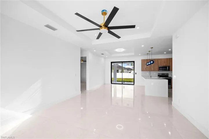 Unfurnished living room featuring a ceiling fan, a tray ceiling, recessed lighting, and light tile patterned floors