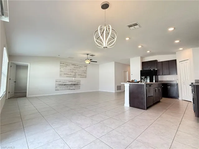 Kitchen with a chandelier, light tile patterned flooring, pendant lighting, open floor plan, and an island with sink