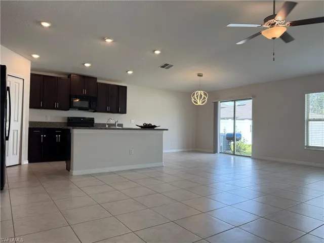 Kitchen featuring an island with sink, black appliances, open floor plan, pendant lighting, and a ceiling fan