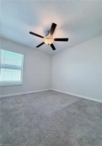 Empty room featuring a textured ceiling, light colored carpet, and ceiling fan