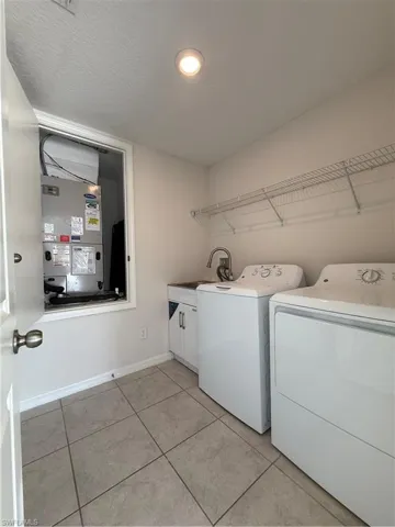 Laundry area featuring light tile patterned flooring, washer and dryer, cabinet space, and a textured ceiling