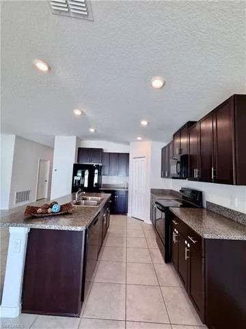 Kitchen with dark brown cabinets, black appliances, a textured ceiling, dark countertops, and light tile patterned flooring