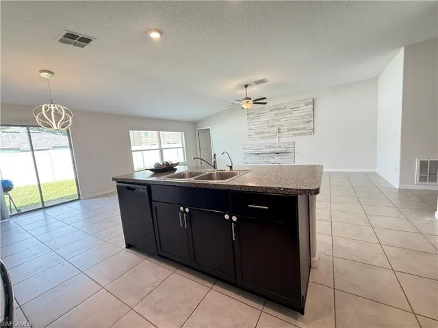 Kitchen with dark cabinetry, open floor plan, a kitchen island with sink, light tile patterned flooring, and a textured ceiling
