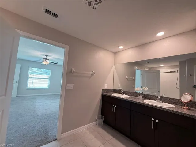 Bathroom featuring double vanity, light tile patterned flooring, tiled shower, and a ceiling fan