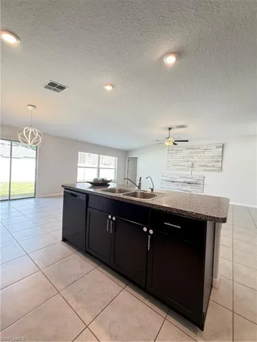 Kitchen with a kitchen island with sink, a textured ceiling, dark cabinets, light tile patterned flooring, and dishwasher