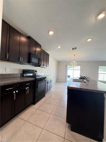 Kitchen featuring dark countertops, stainless steel range oven, an island with sink, black microwave, and pendant lighting