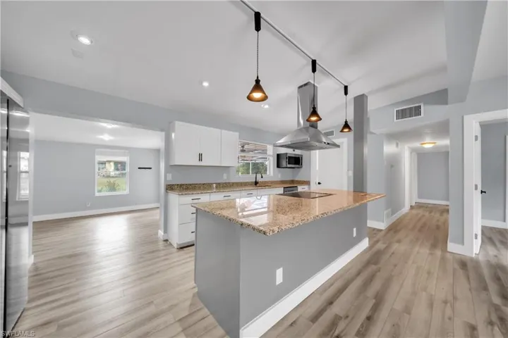 Kitchen featuring rail lighting, light stone counters, white cabinetry, island range hood, and a kitchen island