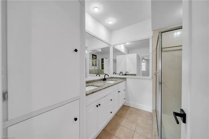 Full bath featuring double vanity, light tile patterned floors, and a shower stall