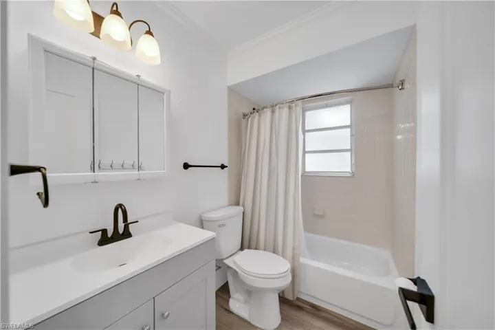 Bathroom with vanity, shower / bath combination with curtain, ornamental molding, and light wood-style flooring