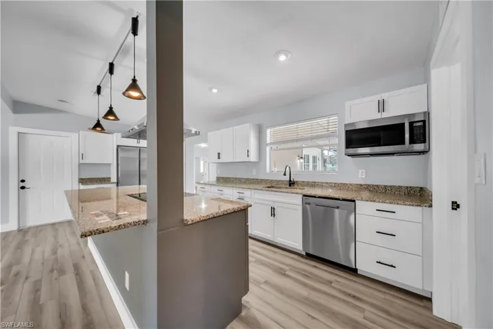 Kitchen with light stone countertops, stainless steel appliances, pendant lighting, a center island, and light wood-type flooring