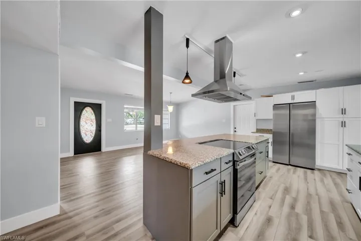 Dual tone kitchen featuring two tone cabinetry, island range hood, stainless steel appliances, light stone counters, and decorative light fixtures