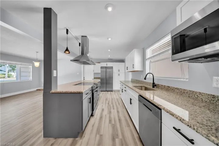 Kitchen featuring stainless steel appliances, light stone counters, island exhaust hood, dual tone cabinets, and decorative light fixtures