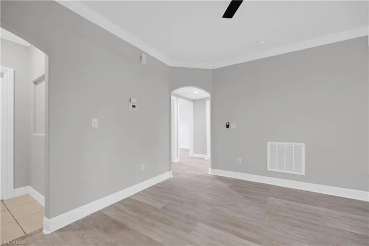 Spacious room featuring wood-finish flooring, light gray walls, white baseboards, and crown molding