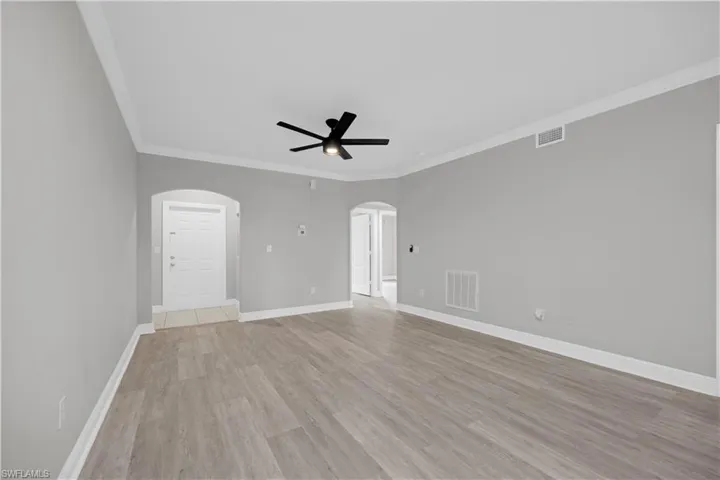 Spacious living area featuring wood-finish flooring, light gray walls, white crown molding, and a black ceiling fan
