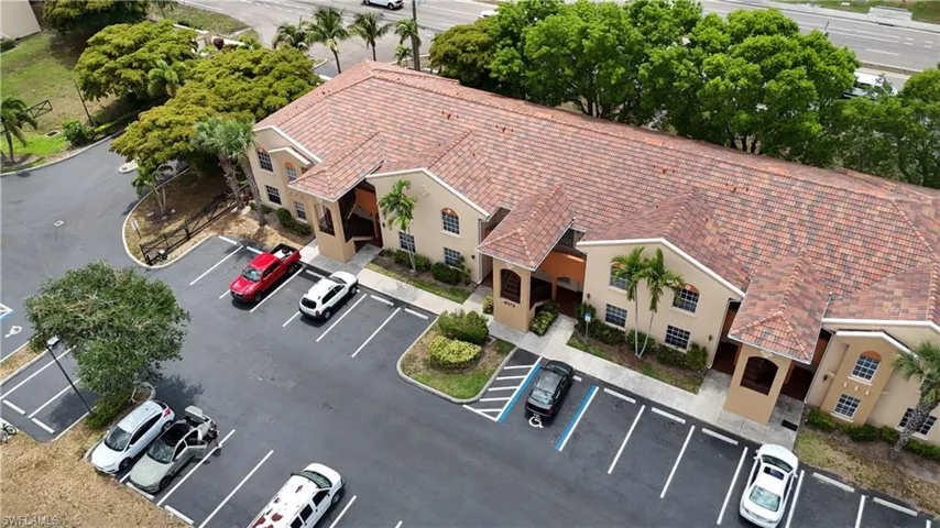 Multi-story building featuring a tile roof, stucco exterior, arched windows, and an onsite parking lot with marked spaces