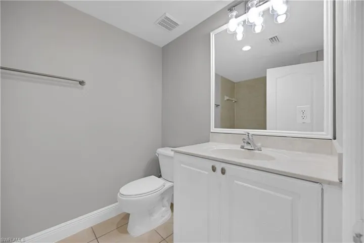 Bathroom featuring a vanity with white cabinetry, an integrated sink, a light-colored countertop, and a framed mirror with overhead lighting