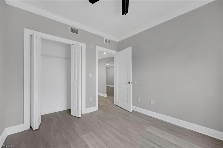 Spacious room featuring light gray walls, wood-finish flooring, white baseboards, and crown molding