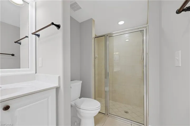 Bathroom featuring a shower with glass enclosure, white tile flooring, and a white vanity with a light-colored countertop