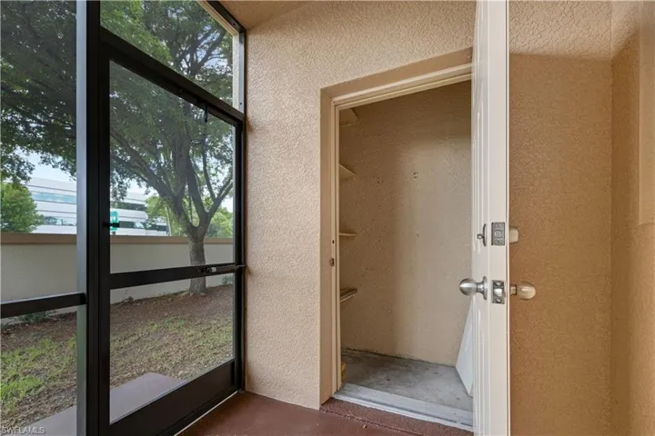 Screened patio area featuring textured walls, exterior storage, and a mature tree visible beyond the screen