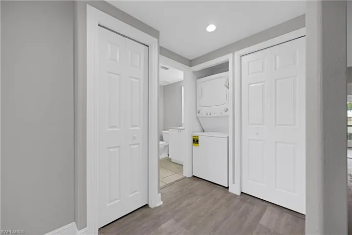 Laundry closet featuring a stacked washer and dryer, wood-finish flooring, and light gray wall paint