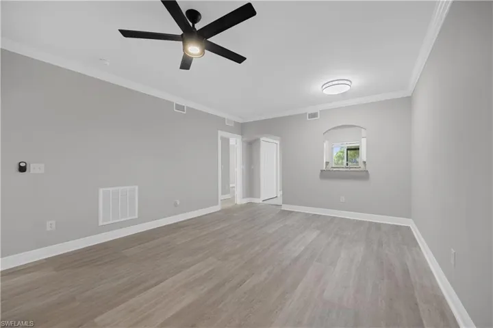 Spacious interior room featuring wood-finish flooring, light gray walls, white crown molding, and a modern ceiling fan