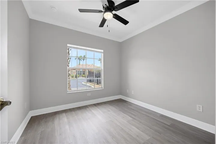 Room featuring wood-finish flooring, light grey walls, white baseboards, and crown molding
