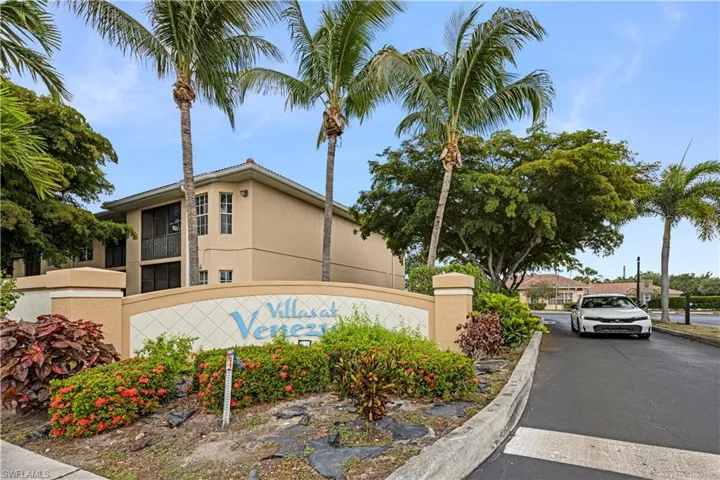 Entryway signage for "Villas at Venezia" with an integrated planter featuring red and green foliage