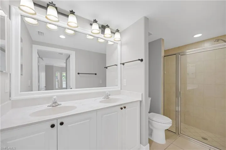 Bathroom featuring a dual vanity with white cabinetry, light-colored countertops, and a large framed mirror with overhead lighting