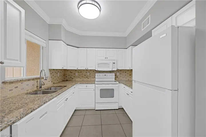 U-shaped kitchen featuring white cabinetry with silver hardware, granite countertops, a double basin sink with a gooseneck faucet, a mosaic tile backsplash, and white appliances