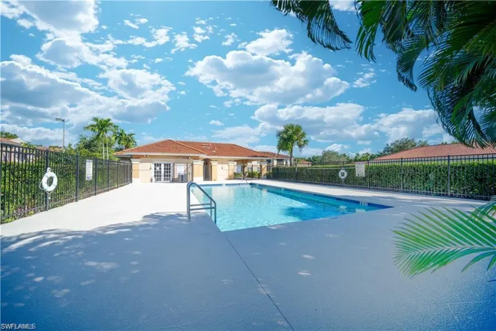 Outdoor swimming pool with a concrete pool deck, surrounded by a black metal fence and mature hedges