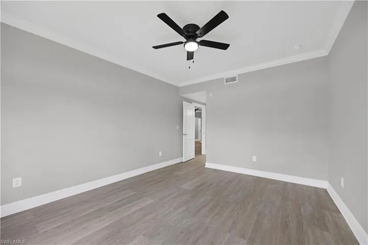 Spacious room featuring wood-finish flooring, light gray walls, white trim, and a contemporary black ceiling fan with integrated lighting