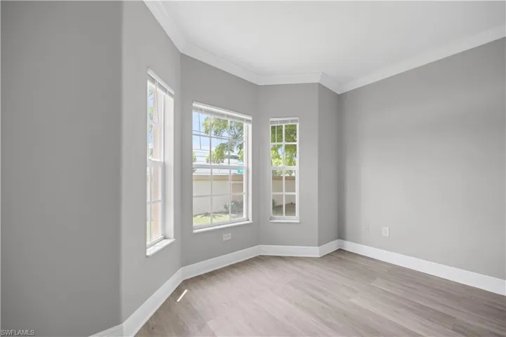 Bay window with multiple white-framed windows, wood-finish flooring, crown molding, and neutral wall tones