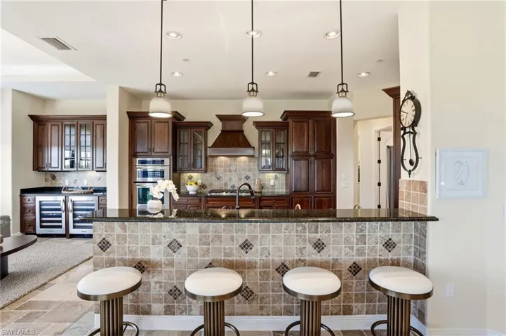 Spacious kitchen featuring gas cook top, 2 wine coolers, bar area, fridge with ice maker, and trash compactor for easy use of the trash chute