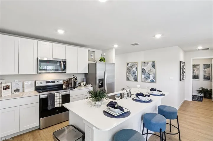 Model home. Kitchen with stainless steel appliances, a breakfast bar, light wood-style floors, an island with sink, and recessed lighting
