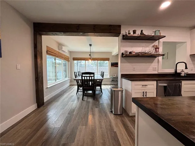 Kitchen featuring white cabinets, hanging light fixtures, dark hardwood / wood-style flooring, stainless steel dishwasher, and an AC wall unit