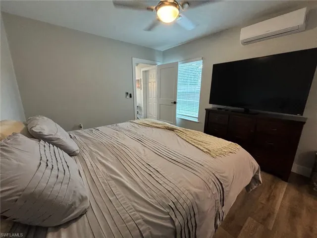 Bedroom with ceiling fan, a wall mounted air conditioner, and dark hardwood / wood-style floors