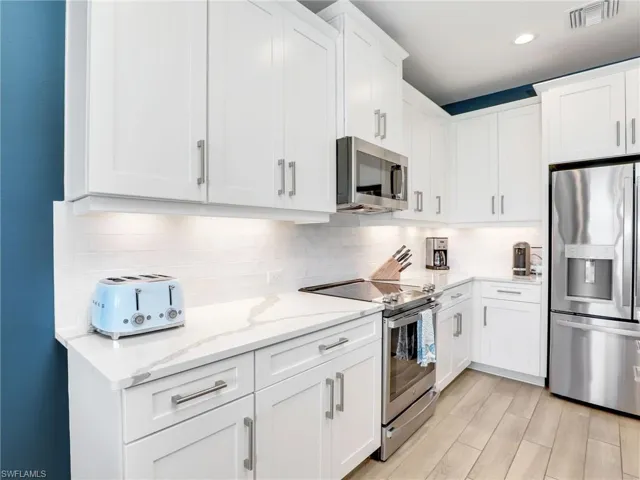 Kitchen with visible vents, white cabinets, decorative backsplash, light stone counters, and stainless steel appliances