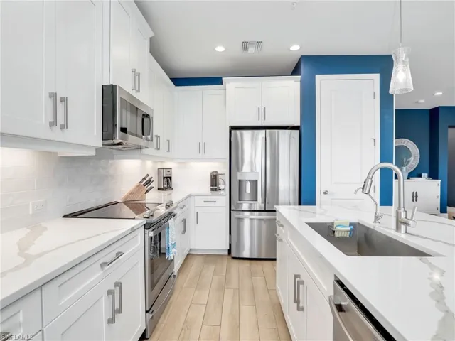 Kitchen with stainless steel appliances, white cabinetry, a sink, and backsplash