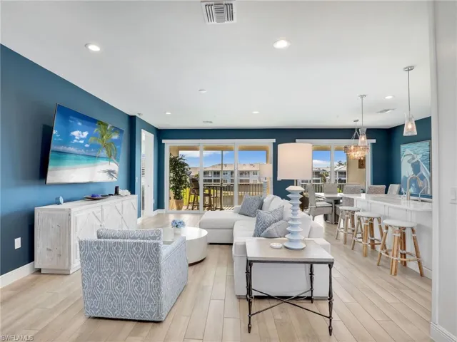 Living area featuring baseboards, light wood-style flooring, visible vents, and a notable chandelier
