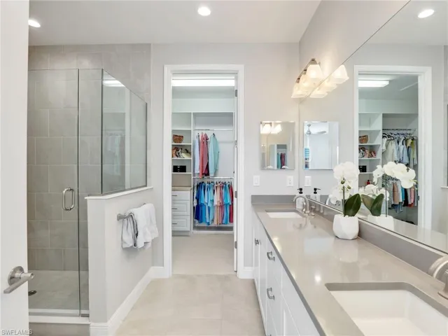 Full bath with double vanity, a shower stall, a sink, and recessed lighting