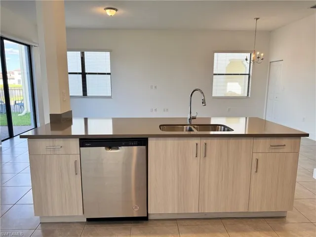 Kitchen featuring sink, stainless steel dishwasher, a center island with sink, and light brown cabinets