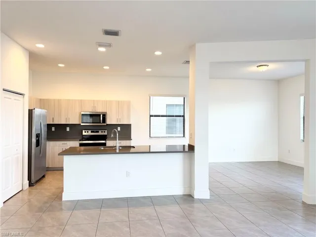 Kitchen featuring light brown cabinets, sink, light tile patterned flooring, kitchen peninsula, and stainless steel appliances