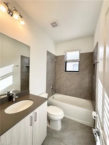 Full bathroom with a textured ceiling, vanity, tiled shower / bath combo, tile patterned flooring, and toilet