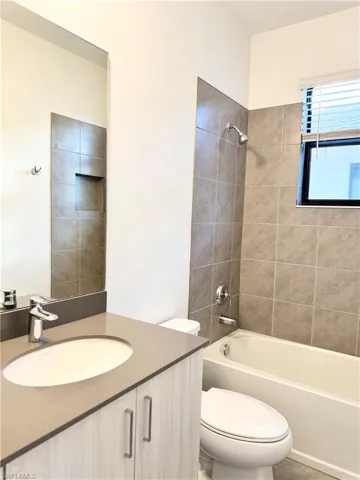 Full bathroom featuring vanity, tiled shower / bath combo, and toilet