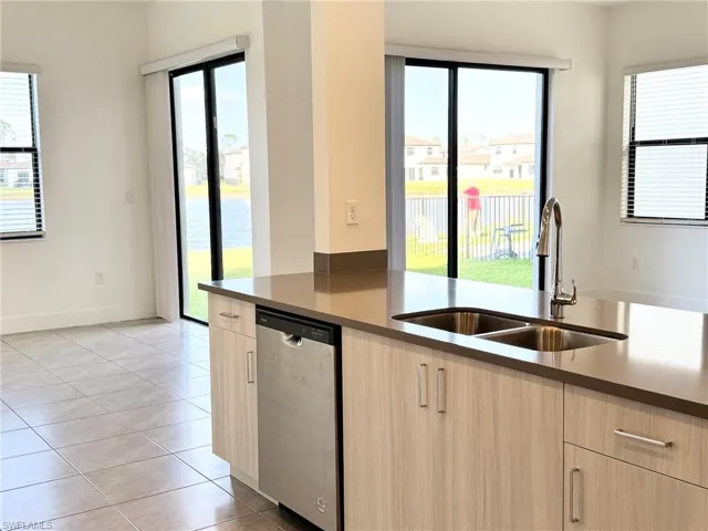 Kitchen with plenty of natural light, stainless steel dishwasher, light brown cabinets, and sink