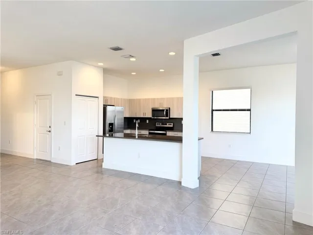 Kitchen with decorative backsplash, appliances with stainless steel finishes, light brown cabinetry, sink, and light tile patterned floors