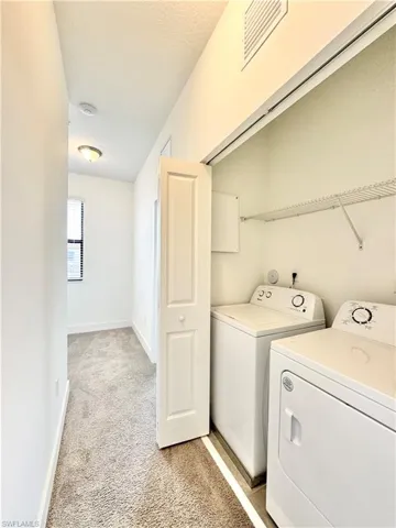 Laundry room with a textured ceiling, washing machine and dryer, and light colored carpet