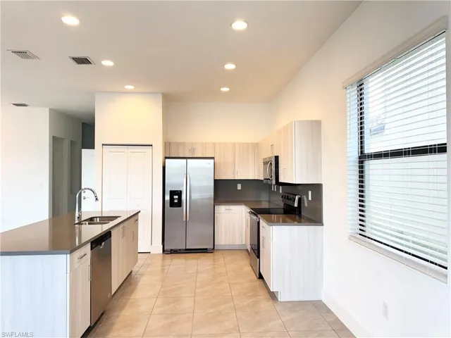 Kitchen featuring light brown cabinetry, sink, light tile patterned flooring, and appliances with stainless steel finishes