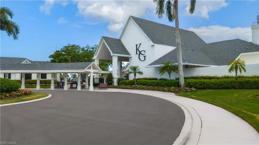 Circular asphalt driveway leading to a covered entrance with white columns and gabled roofs