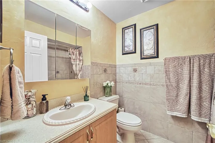 Vanity with integrated sink, wood-finish cabinetry, wall-mounted medicine cabinet, tile wainscoting, and a tiled shower enclosure
